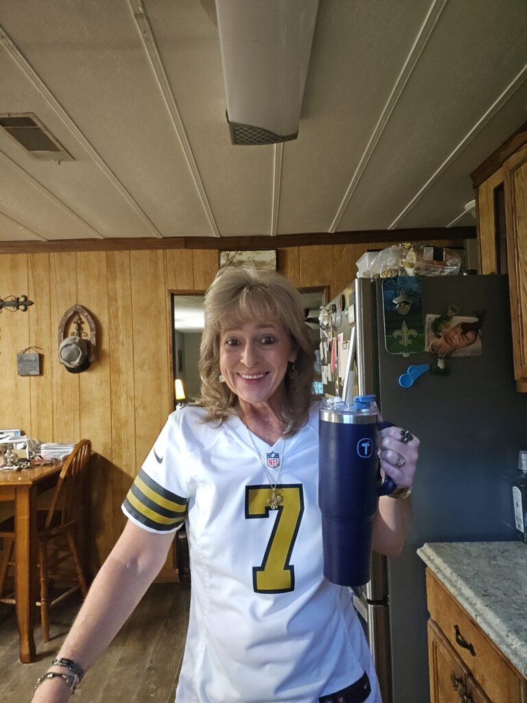 Lisa holding a Big T tumbler in Saints jersey, showing Kitchen Wins On The Move during gameday. 8/17/25