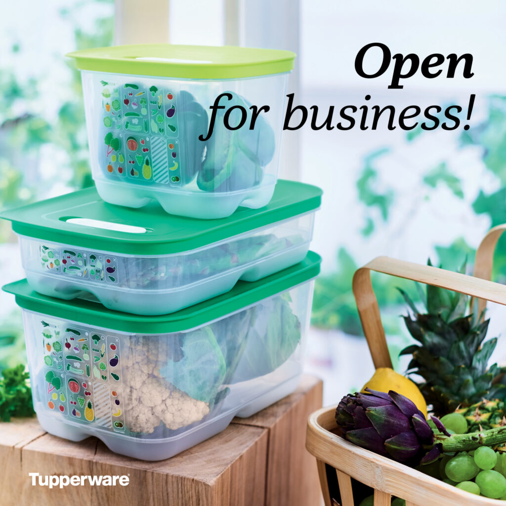 Stacked FridgeSmart containers filled with fresh produce on a wooden surface next to a fruit basket. A popular HOST favorite for keeping party prep fresh and easy.