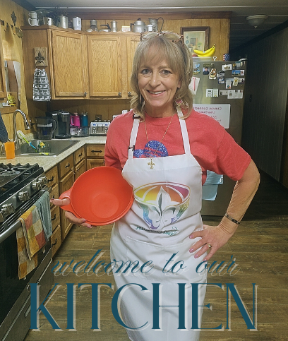 Lisa standing in her cozy Cajun kitchen, smiling while holding a red Tupperware Thatsa bowl and wearing a white apron that reads “Welcome to Our Kitchen” — the heart of the Chaos to Cozy Kitchen System™.