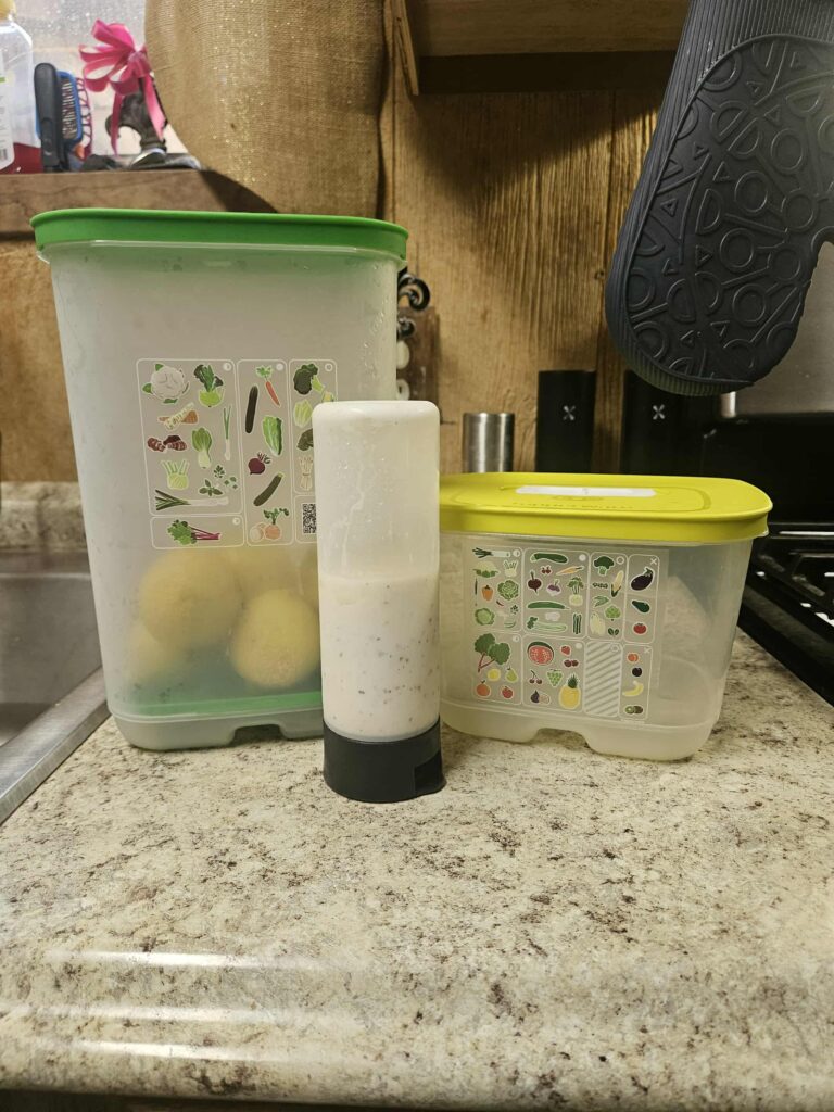 Two Tupperware FridgeSmart containers on the kitchen counter with produce inside, next to a Squeeze-it bottle with dressing.